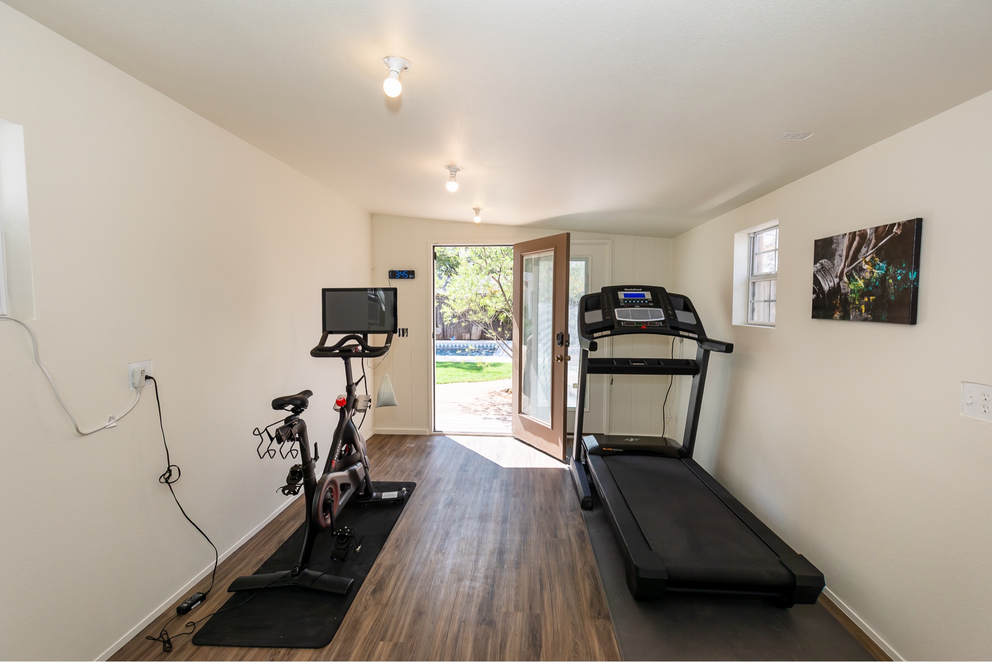 Home gym with Peloton bike, treadmill, and backyard view